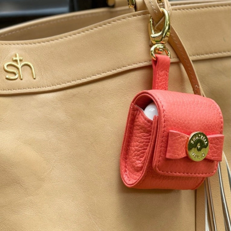 Swatzell + Heilig's AirPod Case in color red, picture showing the clipped onto the side of a tan S + H handbag