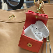 Swatzell + Heilig's AirPod Case in color red, picture showing the clipped onto the side of a tan S + H handbag